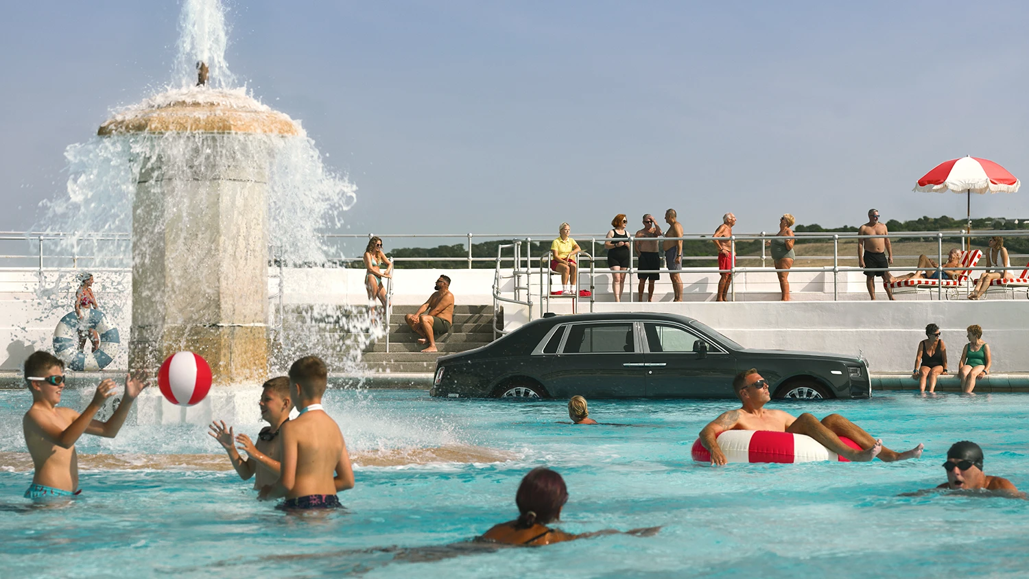 Kąpiący się ludzie w basenie w Plymouth, w którym stoi Rools-Royce Phantom